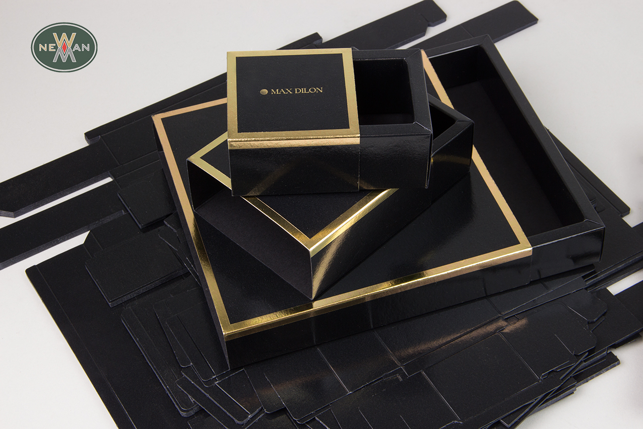 NewMan die-cut sliding boxes with glossy lamination.